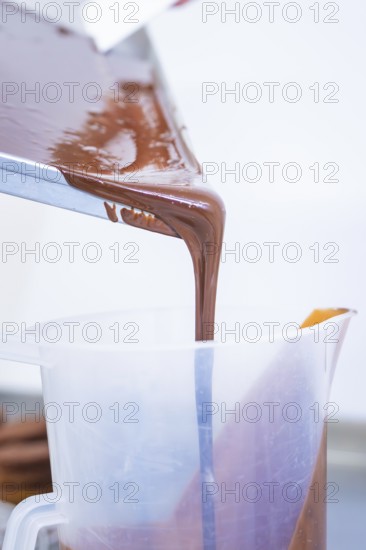 Liquid chocolate is poured from a rectangular container into a plastic container, Vegan Tart Production, Haselstaller Hof, Gechingen, Germany