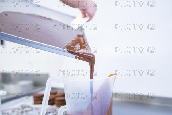 Liquid chocolate is poured from a tray into a large plastic container, presumably in a kitchen, vegan cake production, Haselstaller Hof, Gechingen, Germany
