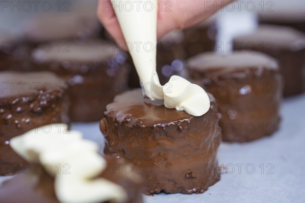Several chocolate cakes are decorated with cream from a piping bag, Vegan Tart Production, Haselstaller Hof, Gechingen, Germany