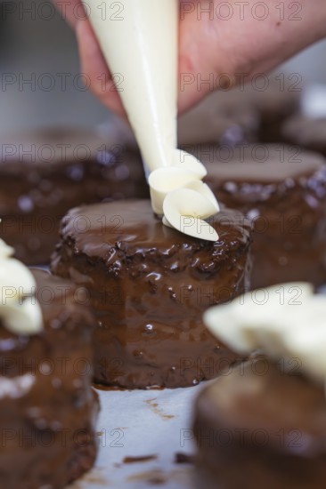 A cake is decorated with cream while several chocolate cakes are waiting, Vegan Tartchen Production, Haselstaller Hof, Gechingen, Germany