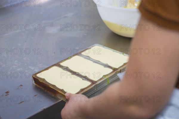 Hands holding chocolate molds in a work area on a table, Vegan Chocolate Production, Haselstaller Hof, Gechingen, Germany