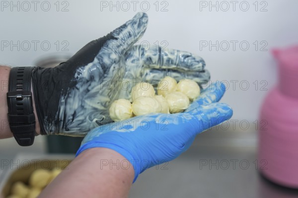 A hand in gloves holds chocolates over a bowl with pink and blue decoration, chocolate quail eggs, Easter production, Haselstaller Hof, Gechingen, Germany
