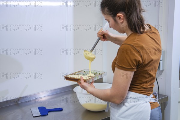 A woman pours chocolate mix into a mold in a kitchen, chocolate quail eggs, Easter production, Haselstaller Hof, Gechingen, Germany