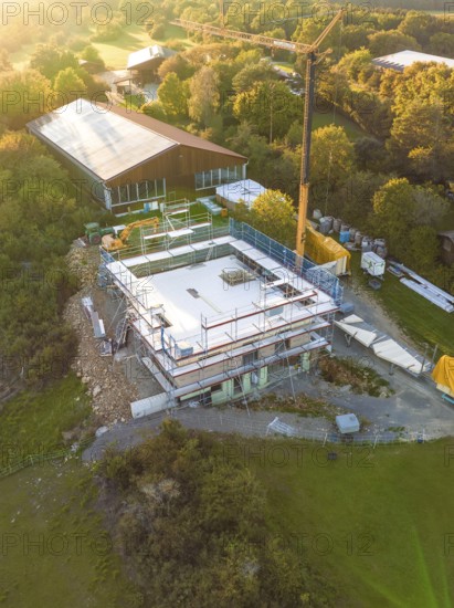 Aerial view of a construction site surrounded by forest and meadows with crane and building structure, timber house construction, Gechingen, Germany