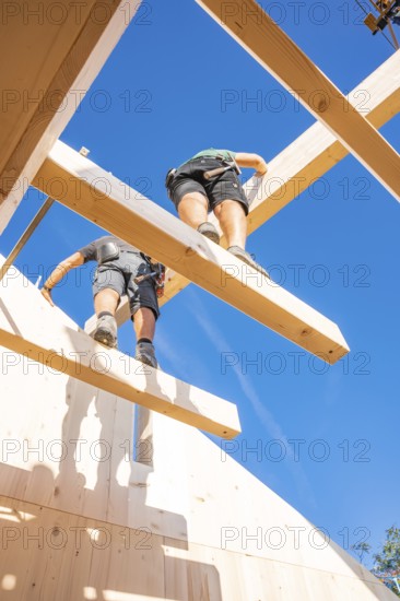 Two construction workers work on wooden scaffolding under a blue sky, Holzhausbau, Gechingen, Germany