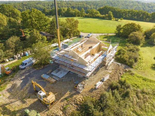 Construction site with timber structure and excavator, surrounded by green landscape and a crane, timber house construction, Gechingen, Germany