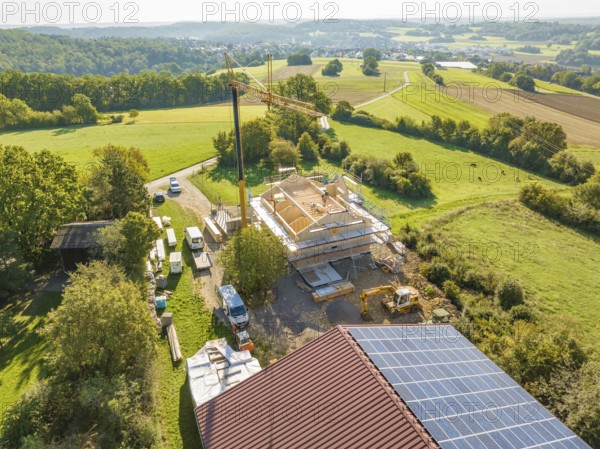 View of construction site with crane and solar panels, surrounded by green countryside and roads, timber house construction, Gechingen, Germany