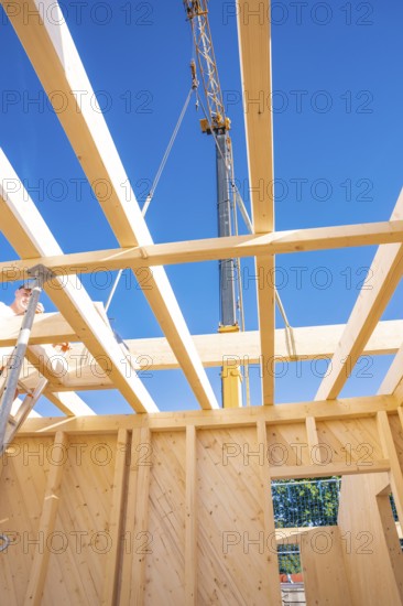 Wooden beams and a crane under a bright blue sky in a construction site, timber house construction, Gechingen, Germany