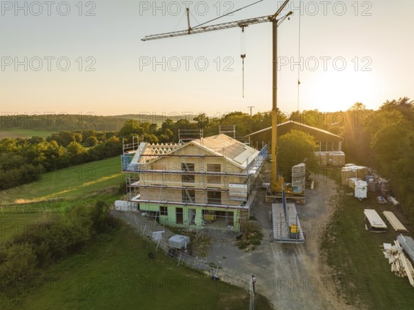 Building under construction, with a crane and scaffolding, in a green setting at sunset, timber house construction, Gechingen, Germany