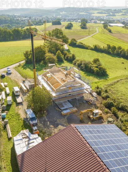 Large construction site with crane in the middle of a green landscape with solar panels on neighboring building, timber house construction, Gechingen, Germany