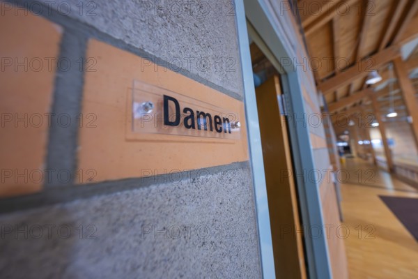 Wall with 'ladies' sign in a room with wooden elements and warm colors, Schlehengäu Sporthalle Gechingen, Calw district, Germany