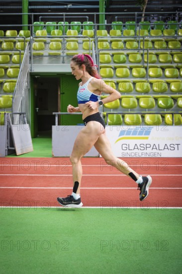 A motivated athlete runs past green stands on an indoor track, middle distance runner Katharina Jaiser, Glaspalast Sindelfingen, Germany