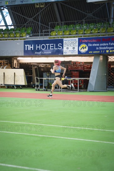 A sporty woman runs at high speed across the green track of a stadium with advertising, middle distance runner Katharina Jaiser, Sindelfingen Glass Palace, Germany