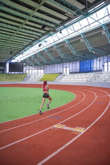 An athlete runs dynamically on a curvy red track in an indoor stadium, middle distance runner Katharina Jaiser, Glaspalast Sindelfingen, Germany