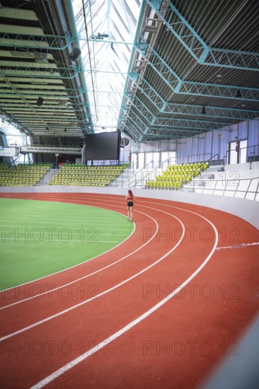 A person runs on an oval, red-green running track of a spacious indoor sports hall, middle distance runner Katharina Jaiser, Glaspalast Sindelfingen, Germany