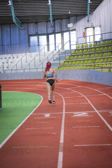 A runner with pink hair jogs on a red track in an indoor stadium, middle distance runner Katharina Jaiser, Glaspalast Sindelfingen, Germany