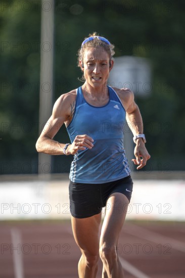 A focused runner on a racetrack wearing a blue sports outfit in sunshine, middle distance runner Katharina Jaiser, Gechingen, Germany
