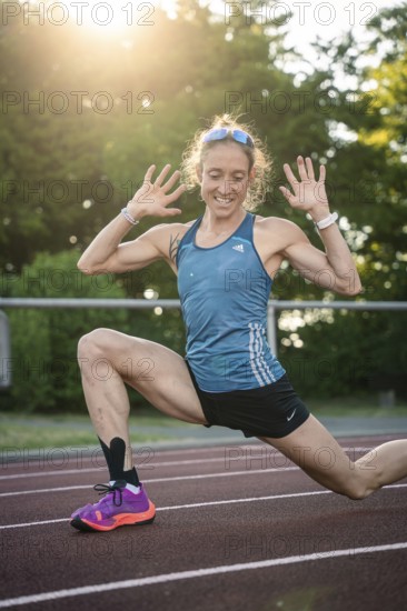 Joyful woman stretching with a smile on the track in sunshine, middle distance runner Katharina Jaiser, Gechingen, Germany