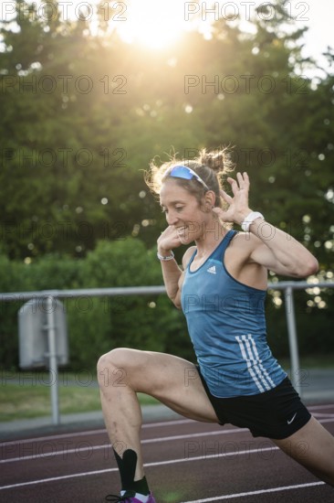 Woman stretching on the track at sunset, concentrated and energetic, middle distance runner Katharina Jaiser, Gechingen, Germany