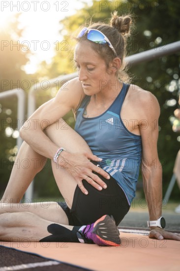 Sporty dressed woman stretching on a running track in summer light, middle distance runner Katharina Jaiser, Gechingen, Germany