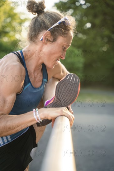 Woman stretches her leg over a barrier, concentrated in warm light and natural scenery, middle distance runner Katharina Jaiser, Gechingen, Germany