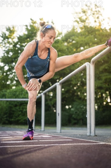 Woman doing intensive stretching on track in sunshine, middle distance runner Katharina Jaiser, Gechingen, Germany