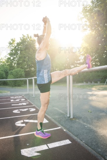 Woman stretches leg on track against bright sunshine, focus on stretching, middle distance runner Katharina Jaiser, Gechingen, Germany