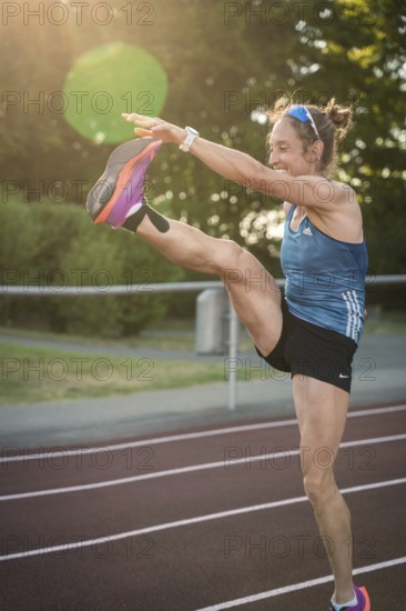 Energetic woman on a running track with a high kick in sunlight, middle distance runner Katharina Jaiser, Gechingen, Germany