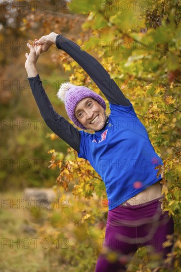 Woman doing stretching exercises in autumn forest, smiling happily surrounded by colorful leaves, middle distance runner Katharina Jaiser, Gechingen, Germany