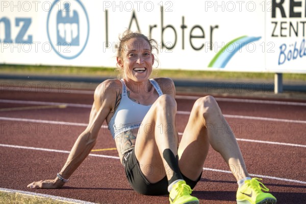 Sportswoman sits exhausted but satisfied on the track, smiling and relaxing, middle distance runner Katharina Jaiser, Gechingen, Germany