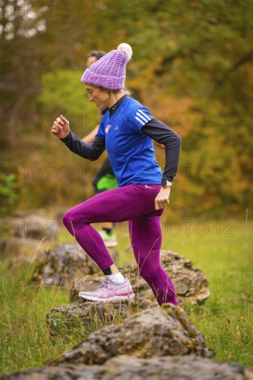 Woman in sporty clothing climbs energetically on rocks in autumn nature, middle distance runner Katharina Jaiser, Gechingen, Germany