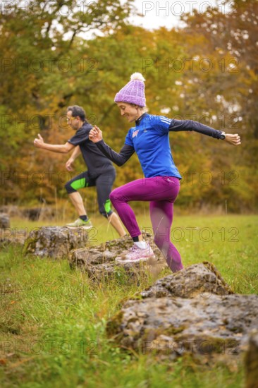 Two people jumping during dynamic training on rocks in autumn forest, middle distance runner Katharina Jaiser, Gechingen, Germany