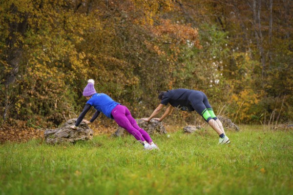 Two people working out outdoors doing push-ups on rocks in an autumn forest, middle distance runner Katharina Jaiser, Gechingen, Germany