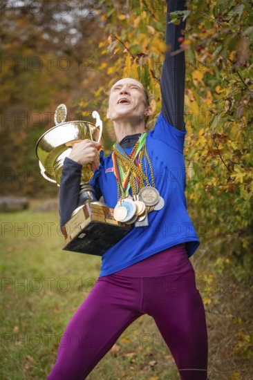 Woman with cup and medals cheers wildly in autumn, middle distance runner Katharina Jaiser, Gechingen, Germany