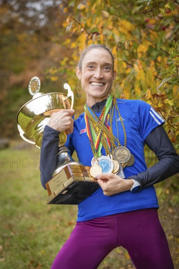 Radiant woman holding a big trophy and many medals in an autumn atmosphere, middle distance runner Katharina Jaiser, Gechingen, Germany