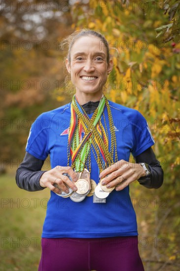 Woman proudly showing her medals in an autumnal setting, middle distance runner Katharina Jaiser, Gechingen, Germany