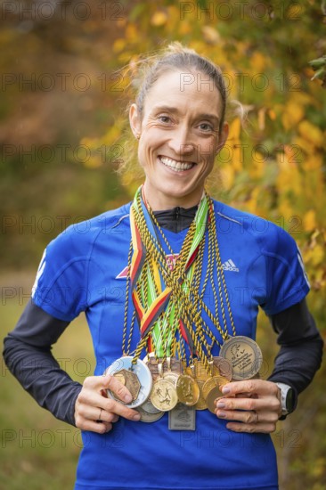 Woman with many medals around her neck smiling in autumn scenery, middle distance runner Katharina Jaiser, Gechingen, Germany
