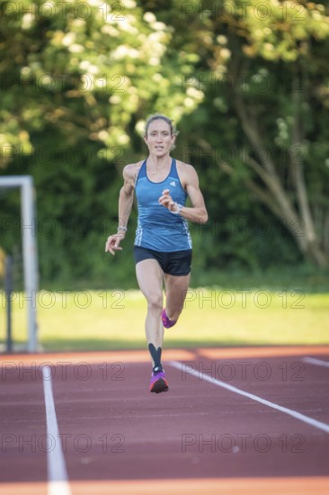 Person running on a red track surrounded by green trees and bright sunlight, middle distance runner Katharina Jaiser, Gechingen, Germany