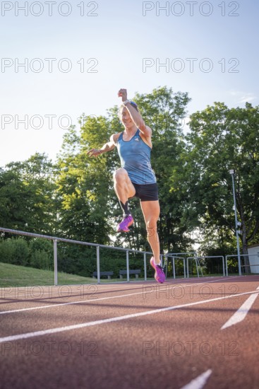 Athlete jumping on a track surrounded by green trees and bright sunshine, middle distance runner Katharina Jaiser, Gechingen, Germany