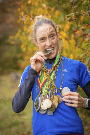 Woman with medals playfully bites on a medal and smiles, middle distance runner Katharina Jaiser, Gechingen, Germany