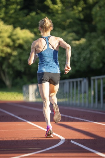 Back view of a running athlete on a red track surrounded by nature, middle distance runner Katharina Jaiser, Gechingen, Germany