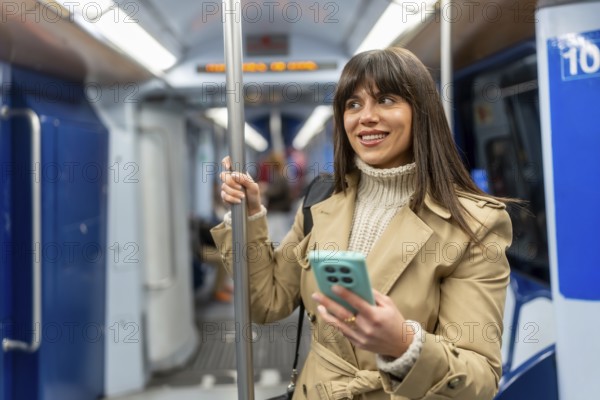 Young woman standing inside a modern subway train, holding onto a pole while checking her smartphone and smiling, representing urban daily commute and connection