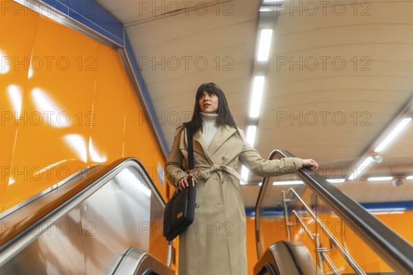 Woman travelling on an escalator in a subway station, holding onto the handrail, dressed in a trench coat, reflecting urban movement, daily routine, and public transportation