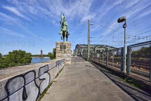 Equestrian statue of Emperor Frederick III, Hohenzollern Bridge, arched bridge, steel arches, metal fence, sandstone wall, catenary masts, overhead lines, lantern, graffiti, footpath made of paving slabs, trees, blue sky, cirrus clouds, Cologne, district-free city, North Rhine-Westphalia, Germany