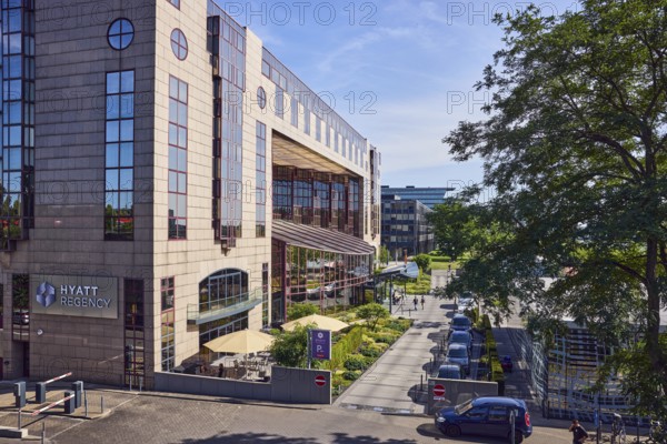Hyatt Regency, hotel, commercial building, modern architecture, general development, parking strip with cars, flower bed, lawn, trees, elevated perspective, blue sky, cirrus clouds, cirrostratus clouds, Kennedy shore, Cologne, district-free city, North Rhine-Westphalia, Germany