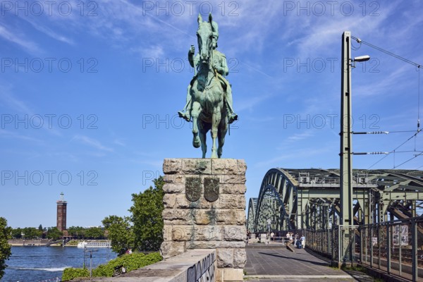 Emperor Frederick III, equestrian statue, sandstone wall, pedestrian and railway bridge, bridge, arched bridge, steel arches, metal fence, catenary masts, overhead lines, footpath made of paving slabs, Rhine river, exhibition tower, pedestrians as a secondary motif, trees, blue sky, cirrus clouds, Hohenzollern bridge, Cologne, district-free city, North Rhine-Westphalia, Germany