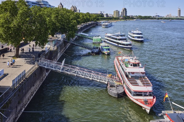 Rhine river, general architecture, Zoobrücke car bridge, footpath and cycle path, waterfront, boat launch, gangway, wharf, excursion boats, pedestrians as accessories, trees, bird's-eye view, blue sky, cloudless, potion yard, Cologne, district-free city, North Rhine-Westphalia, Germany