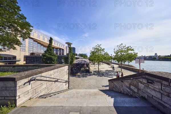 Staircase, natural stone wall, waterfront, Rhine river, commercial building, modern architecture, lantern, city trees, cyclists and pedestrians as a secondary motif, blue sky, cirrus clouds, cirrostratus clouds, Kennedy shore, Cologne, district-free city, North Rhine-Westphalia, Germany