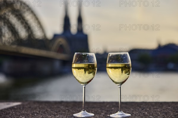 Wine glasses, wine, light refraction in filled glasses, concrete wall, Rhine river, Hohenzollern bridge, arched bridge, steel arches, Cologne Cathedral, double tower, general architecture, depth of focus, sharp foreground - background blurred, sunset, red and orange sky, cirrostratus clouds, Cologne, district-free city, North Rhine-Westphalia, Germany