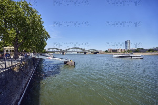Rhine river, sightseeing boats, total view, general architecture, high-rise buildings, pedestrian and railway bridge Hohenzollern Bridge, arched bridge, steel arches, pier, gangway, quay wall, waterfront, trees, blue sky, cloudless, Leystapelwerft, Cologne, district-free city, North Rhine-Westphalia, Germany